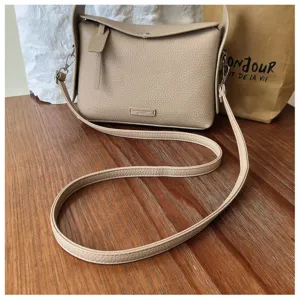 Close-up detail of beige leather crossbody shoulder bag with fine texture and metal hardware.