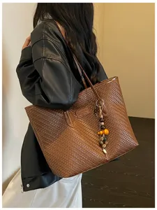 Détail du sac cabas tressé marron avec une texture en cuir fin et un pendentif chic.