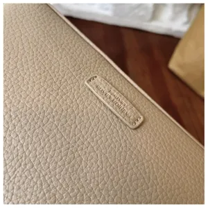 Close-up detail of beige pebbled leather crossbody bag showing delicate texture and label.