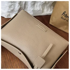 Detailed shot of minimalist leather crossbody bag in khaki with pebbled texture and flap design.