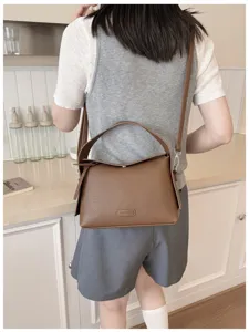 Detail shot of the brown leather shoulder bag, showcasing premium texture and side handle design.