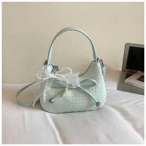 Light green woven crescent shoulder bag with elegant pearl bow detail, chic style detail.