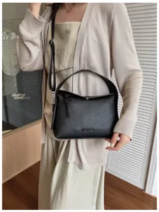 Detailed view of the stylish black leather shoulder bag with top handle worn by a model.