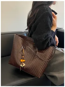 Vue détaillée élégante du sac cabas tressé en cuir marron foncé avec joli pendentif.