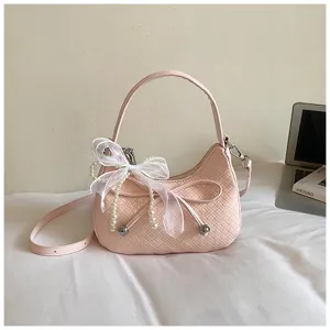 Pink woven crescent shoulder bag with white pearl bow pendant detail for chic daily style.