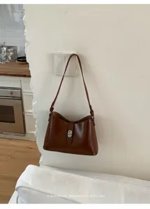 Dettaglio borsa a spalla minimalista in pelle marrone con elegante chiusura in metallo.