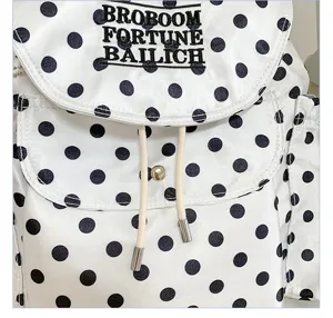 Black and white polka dot backpack detail showing embroidered letters, flap and drawstring.