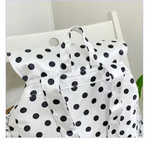 Detail shot of a trendy white and black polka dot backpack, showing straps and classic pattern.