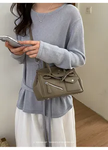 Detailed view of the stylish greyish-brown shoulder bag with zipper pocket and metal clasp.