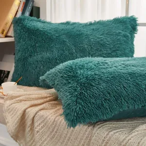 Nahaufnahme von flauschigen türkisen Zierkissen mit langem Fell auf einer Decke.
