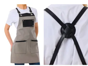 Detailed view of grey canvas apron with black leather straps and pockets for work kitchen.