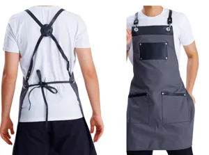 Grey canvas work apron with leather straps, cross back design and multiple utility pockets.