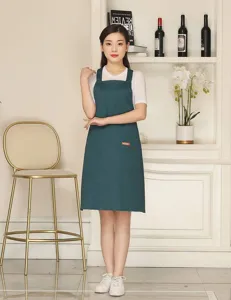 Detailed view of the dark green cotton blend apron with cross back straps and front pocket.