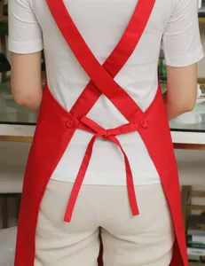 Detailed view of red cross-back apron showing adjustable straps and buttons for workwear use.