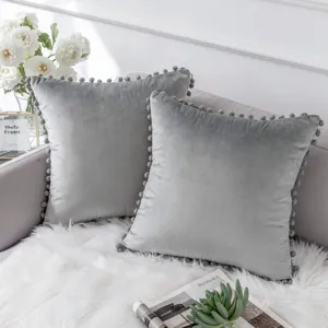 Graues Samtkissen mit Pompons Detail auf dem Wohnzimmersofa in gemütlicher Deko Szene.