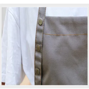 Gros plan détaillé du tablier en toile de coton grise avec boutons pression et belles finitions.