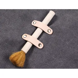 Brosse de nettoyage en bois avec lanière en cuir et rivets pour tabliers de travail en toile.