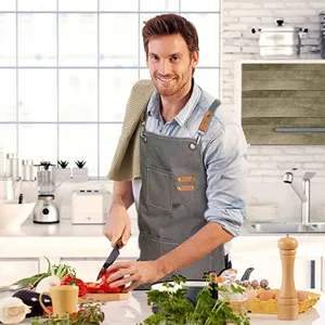 Grey canvas apron with leather straps and pockets, ideal for kitchen cooking and workshop use.