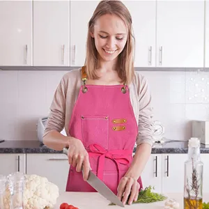Pink canvas kitchen apron with leather straps and pockets for cooking and gardening.