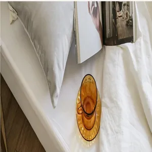 Detail view of the soft gray plush throw pillow on a white bed with a glass cup and magazine.