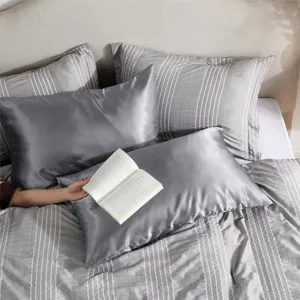 Taie d'oreiller en satin gris et parure de lit rayée pour une décoration de chambre élégante.
