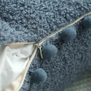 Close-up detail of blue teddy fleece cushion cover with pom pom trim and zipper.