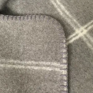 Close-up detail of grey knitted wool throw blanket with white grid pattern and purple stitched edge.
