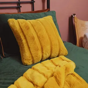 Close-up detail of soft yellow plush striped throw pillow and cozy blanket in bedroom.