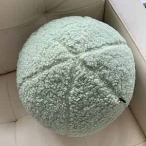 Close-up detail of the light green teddy fleece round ball pillow on a cozy sofa cushion.