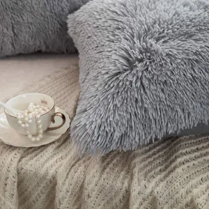 Nahaufnahme eines weichen grauen Zottel-Plüschkissens auf einer gemütlichen Strickdecke.