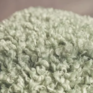 Close-up detail of light green fluffy curly boucle cushion cover texture fabric soft cozy.