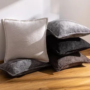 Vue de détail de coussins texturés en chenille empilés sur sol en bois pour canapé de salon.