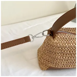 Primer plano detallado del bolso de hombro de paja tejida con correa de cuero marrón y metal.