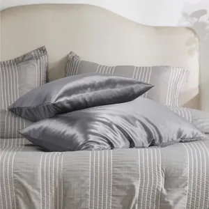 Détail de coussin de corps en satin montrant une texture soyeuse et une couleur grise.