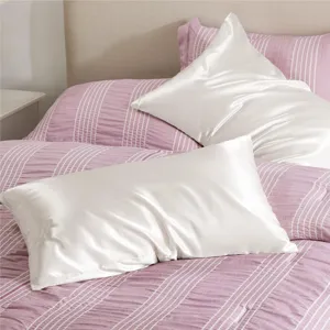 Taie d'oreiller en satin blanc associée à une parure de lit rayée rose, texture douce.