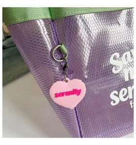 Clear transparent PVC tote bag with green handles and cute pink heart keychain for daily use.