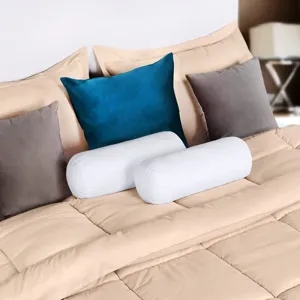 Close-up detail of cozy cylindrical bolster pillows and decorative cushions on bed set.