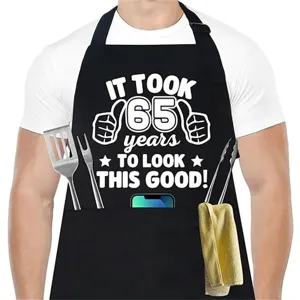 Vista detallada del delantal de cocina negro con divertido estampado de 65 años y bolsillos.