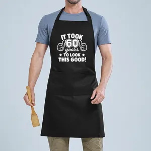 Black cotton kitchen apron detail showing funny 60th birthday quote print and convenient front pocket.
