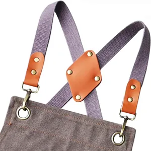 Close-up detail of sturdy canvas apron cross straps with brown leather and metal hardware.
