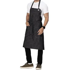 Men's dark denim work apron detail showing cross-back strap, chest pocket and waist ties.