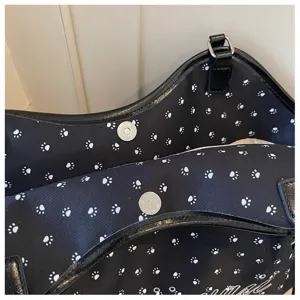 Détail en gros plan du sac noir avec des empreintes de pattes blanches et bouton aimanté.