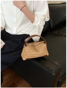 Vista detallada del elegante bolso de mano tejido de paja con asa de cuero y cierre metálico.