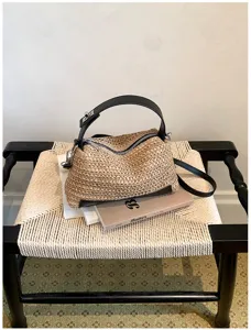 Detalle del elegante bolso de hombro de paja tejida con asa de cuero negro y cremallera.