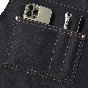 Close-up detail of dark canvas work apron front utility pocket holding phone and small tools.
