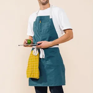Vista detallada del delantal de cocina azul verdoso con tirantes blancos y bolsillo.