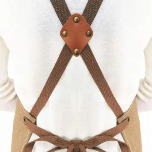 Detail shot of cross-back canvas apron with leather patch and metal rivets for kitchen cooking.