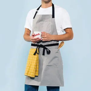 Detalle del delantal de trabajo de lona gris, con tirantes negros duraderos y bolsillos prácticos.