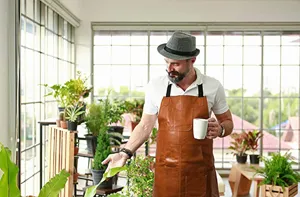 Detail view of a brown PU leather apron with pockets in a bright plant greenhouse setting.