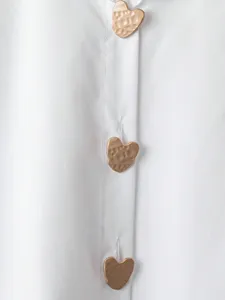 Primo piano dettaglio di camicia bianca manica lunga con bottoni a cuore in metallo.